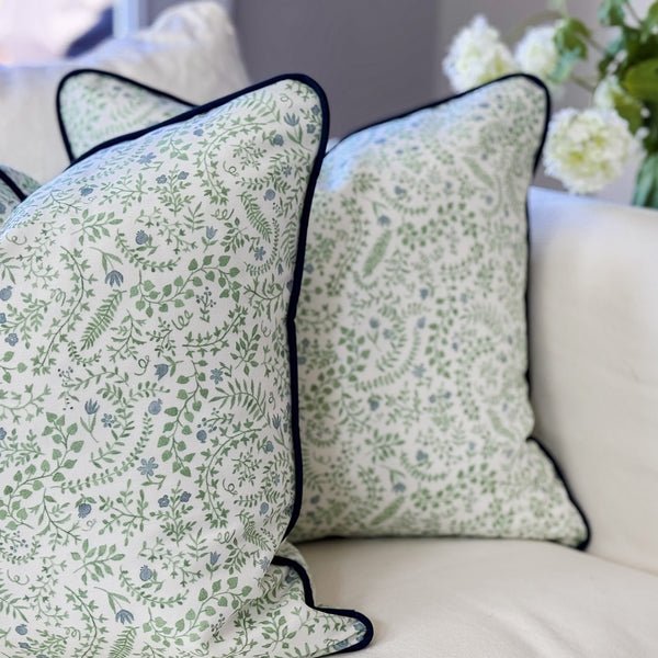 Floral patterned pillows on a sofa with a vase of flowers in the background