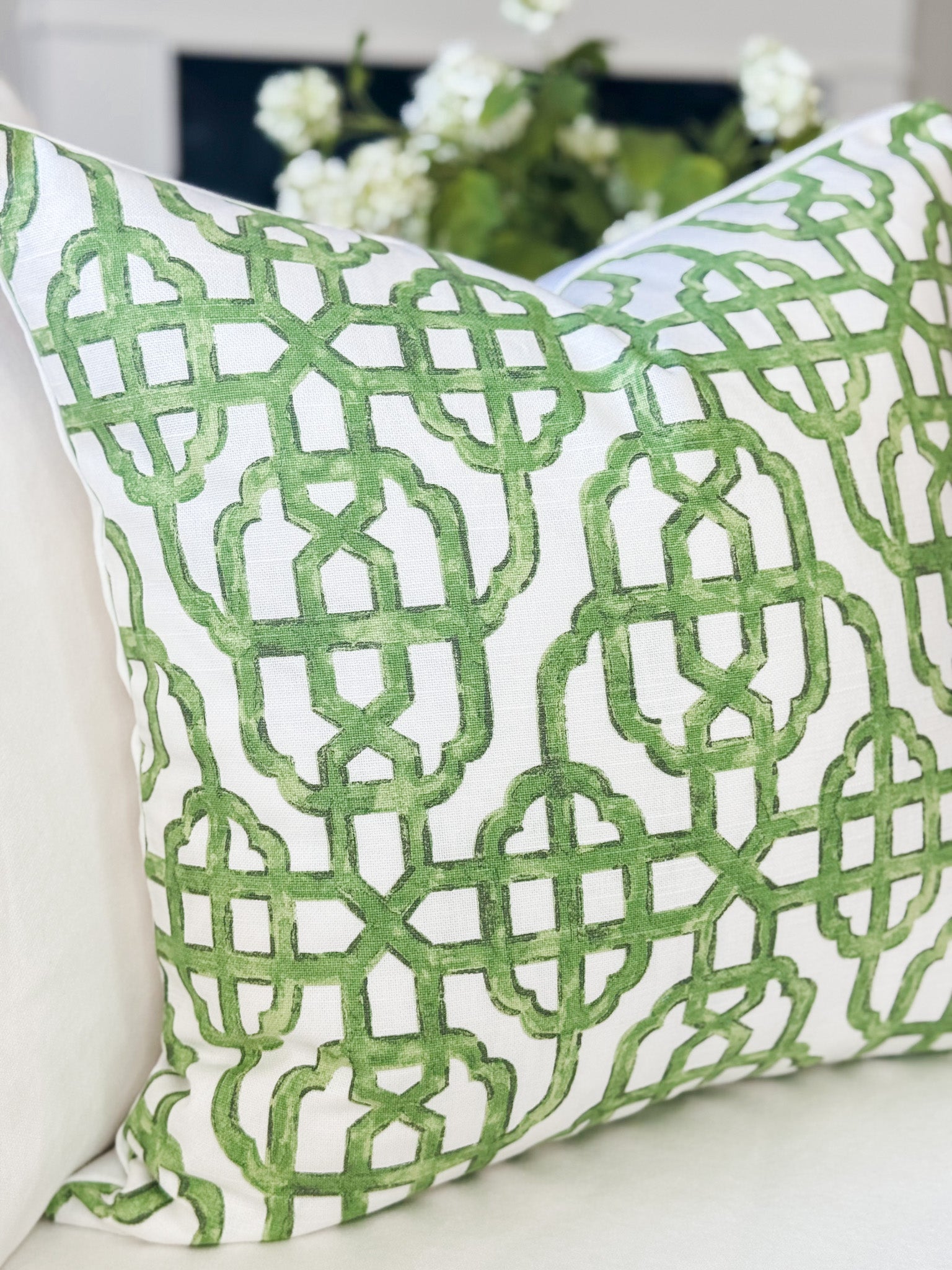 Green and white patterned pillow on a white surface with a blurred background