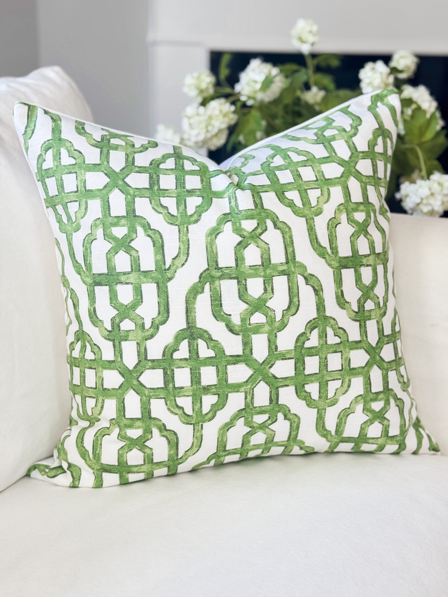 Green patterned pillow on a white couch with flowers in the background