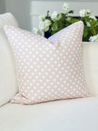 Pink patterned pillow on a beige sofa with white flowers in the background