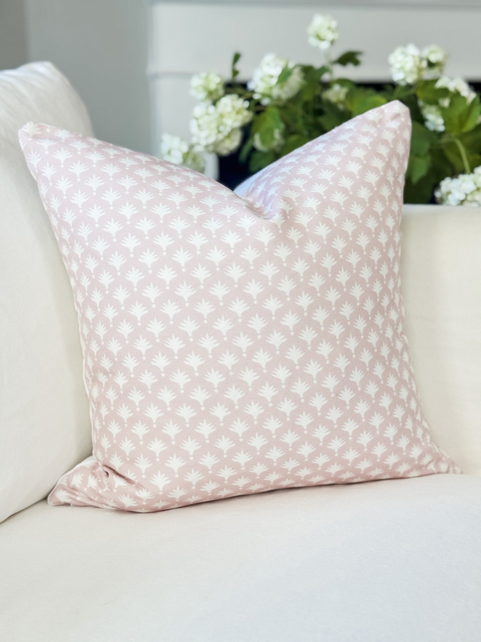 Pink patterned pillow on a beige sofa with white flowers in the background