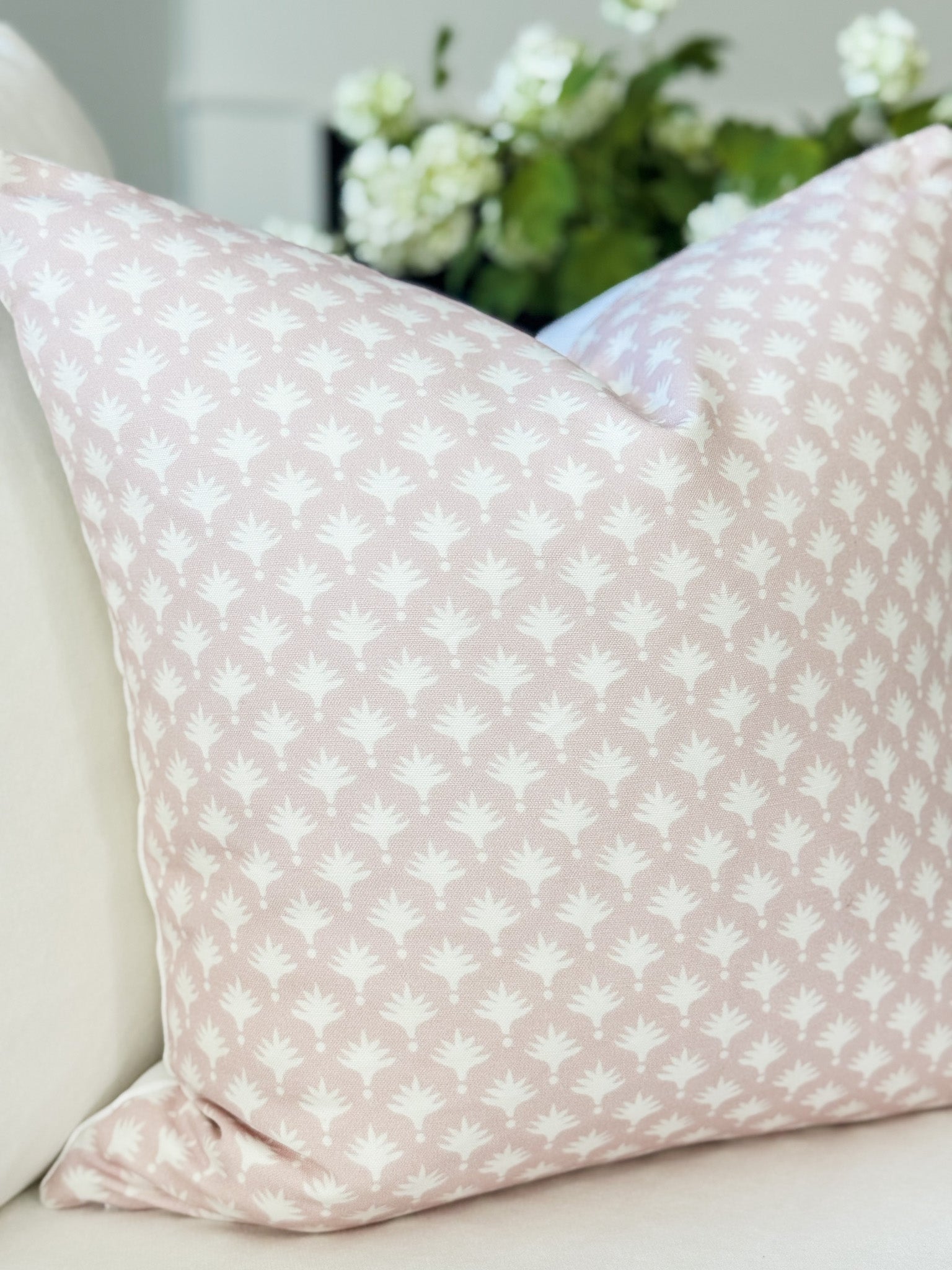 Pink pillow with white floral pattern on a light-colored couch with flowers in the background