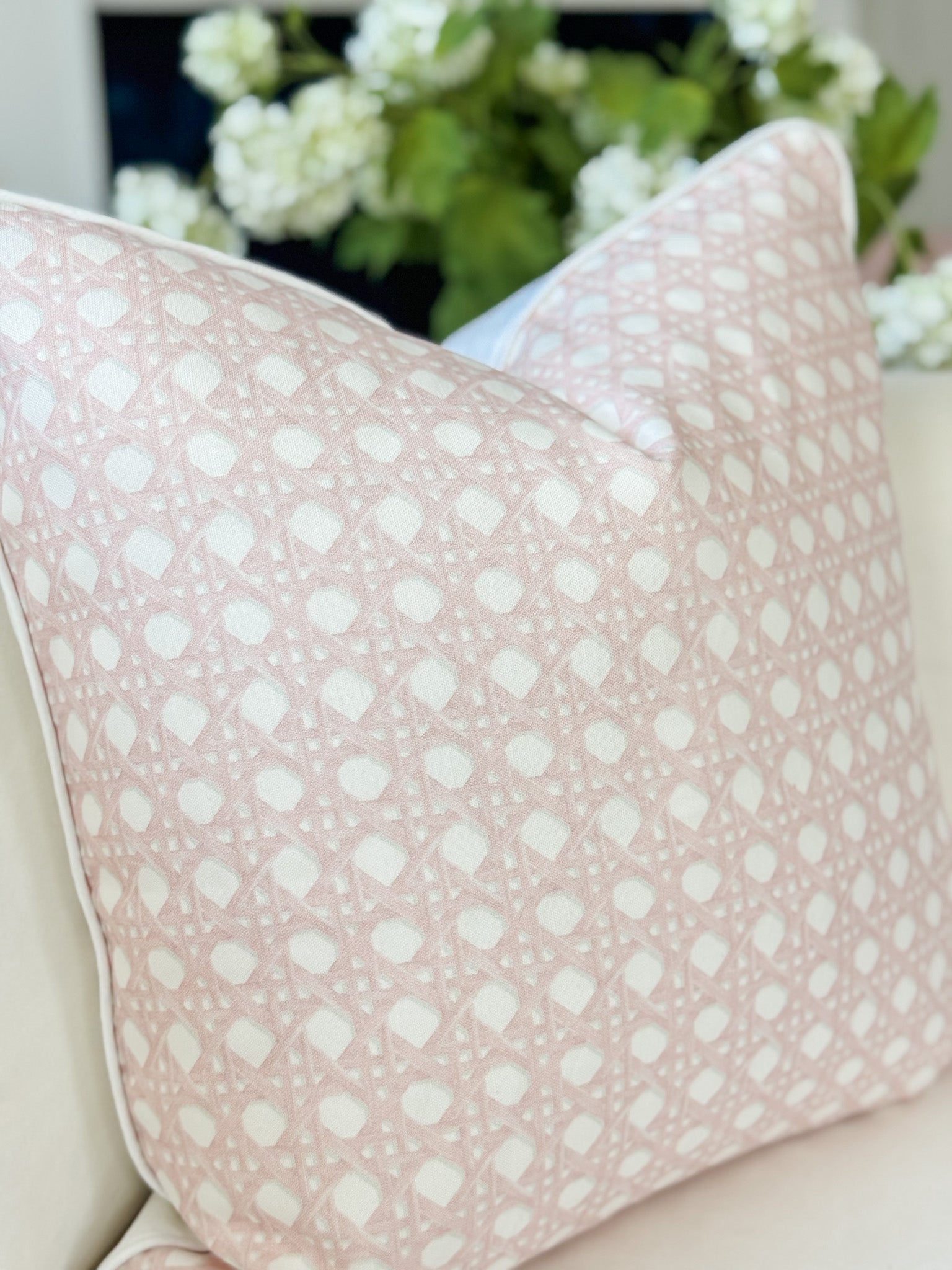 Pink pillow with white polka dots on a beige couch with a blurred floral background