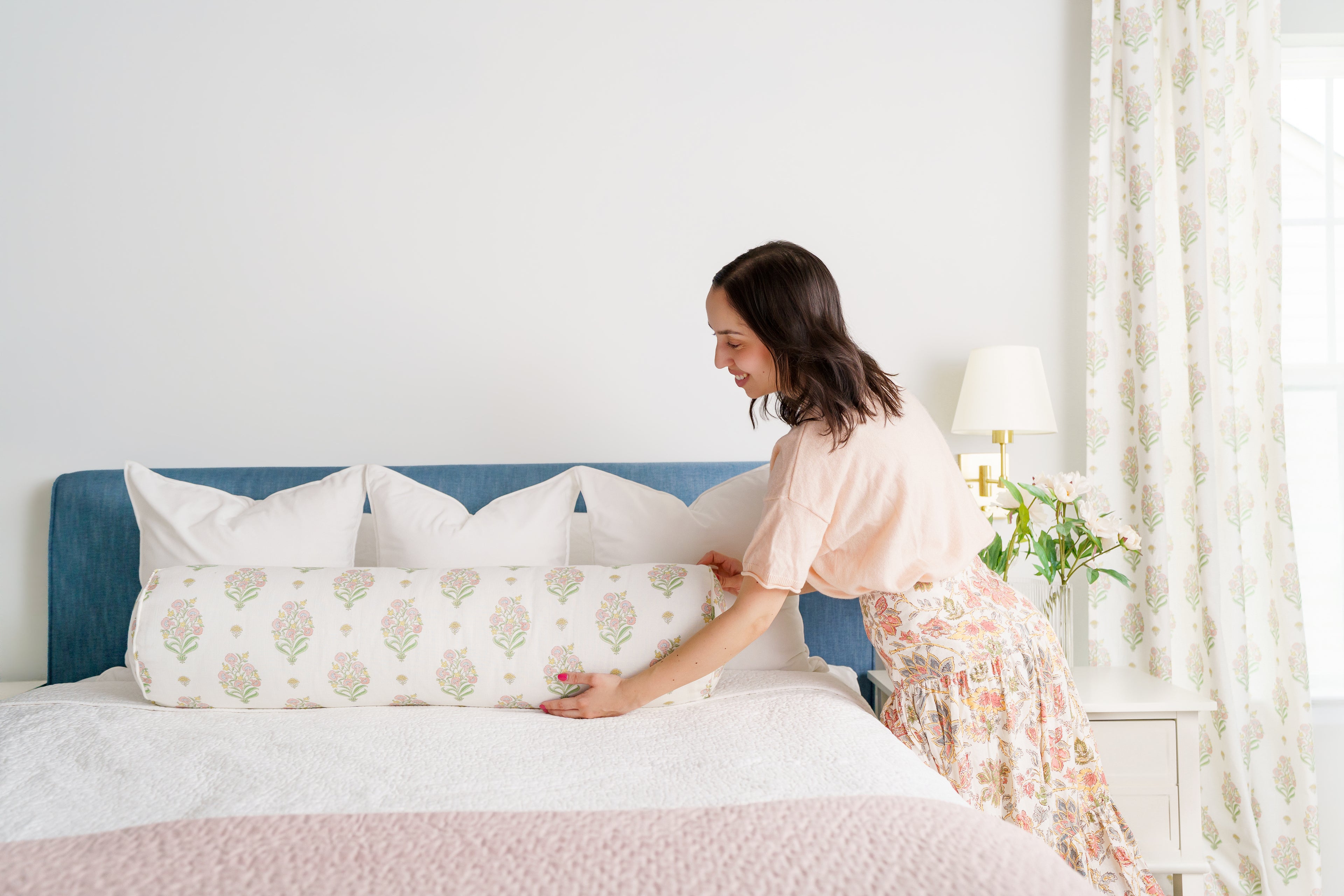 Woman arranging pink and green bolster pillow on a bed in a bright bedroom